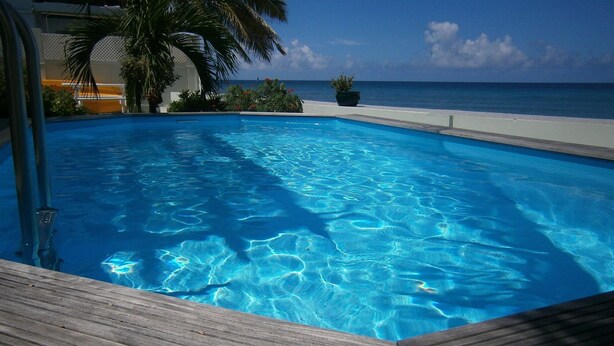 Una piscina azul cristalina con una cubierta de madera, rodeada de follaje y vistas al océano.