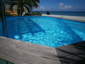 A clear blue pool with a wooden deck, surrounded by greenery and a view of the ocean. - 3 BR/3 bath. Sint Maarten DIRECT BEACHFRONT & PRIVATE POOL!  
From 250/nt!! (Beacon Hill)
