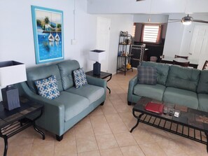 A living room with a sofa, a coffee table, a painting, and a dining area with chairs and a table.