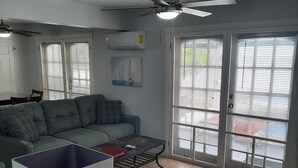 Una sala de estar con sofá, una mesa de centro, ventilador de techo y puerta corrediza de vidrio que da a un área exterior.