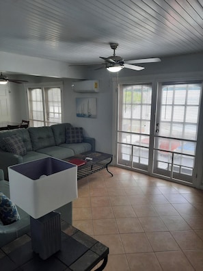 A living room with a sofa, a coffee table, a ceiling fan, and a sliding glass door leading to an outdoor area.