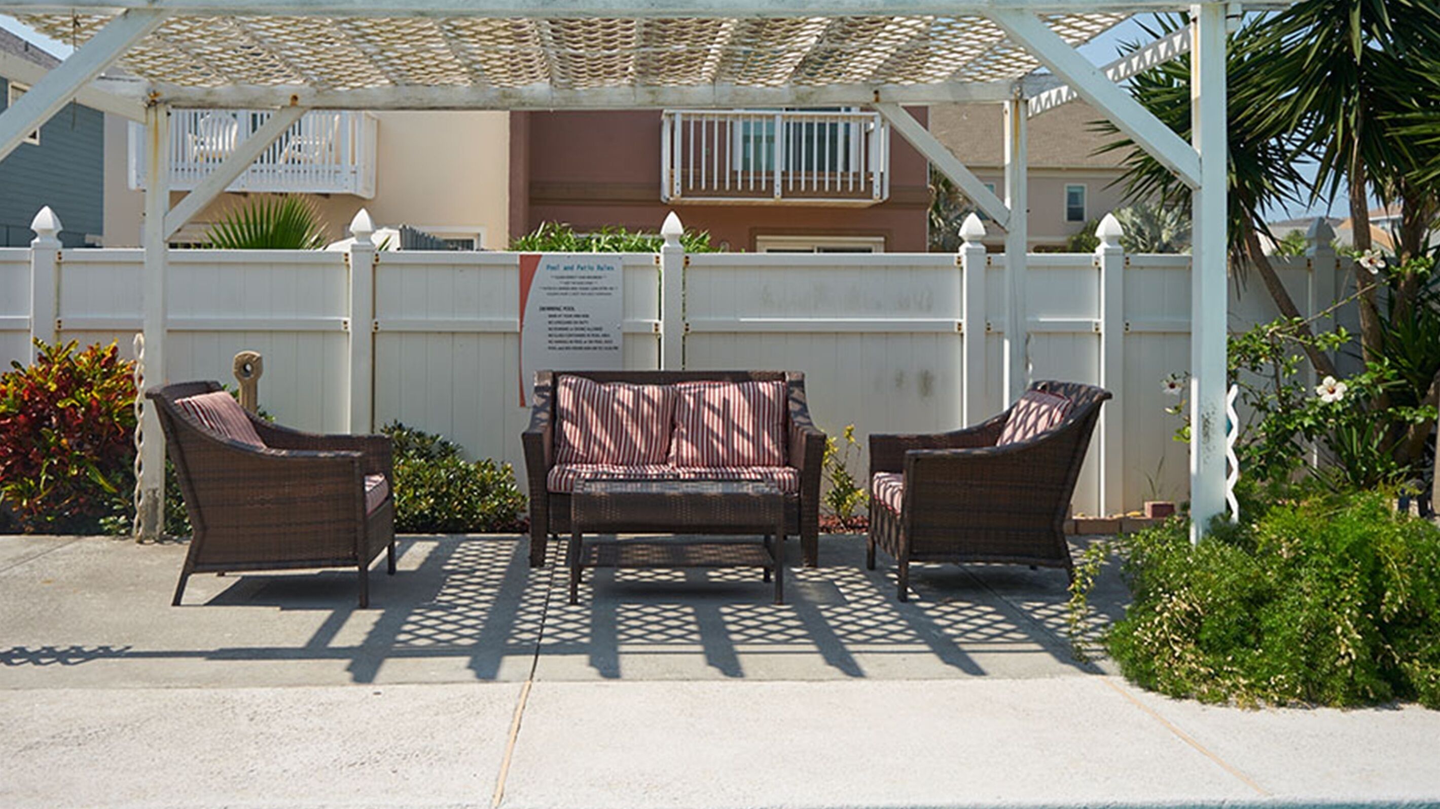 Een overdekt terras met rieten meubilair en een pergola.