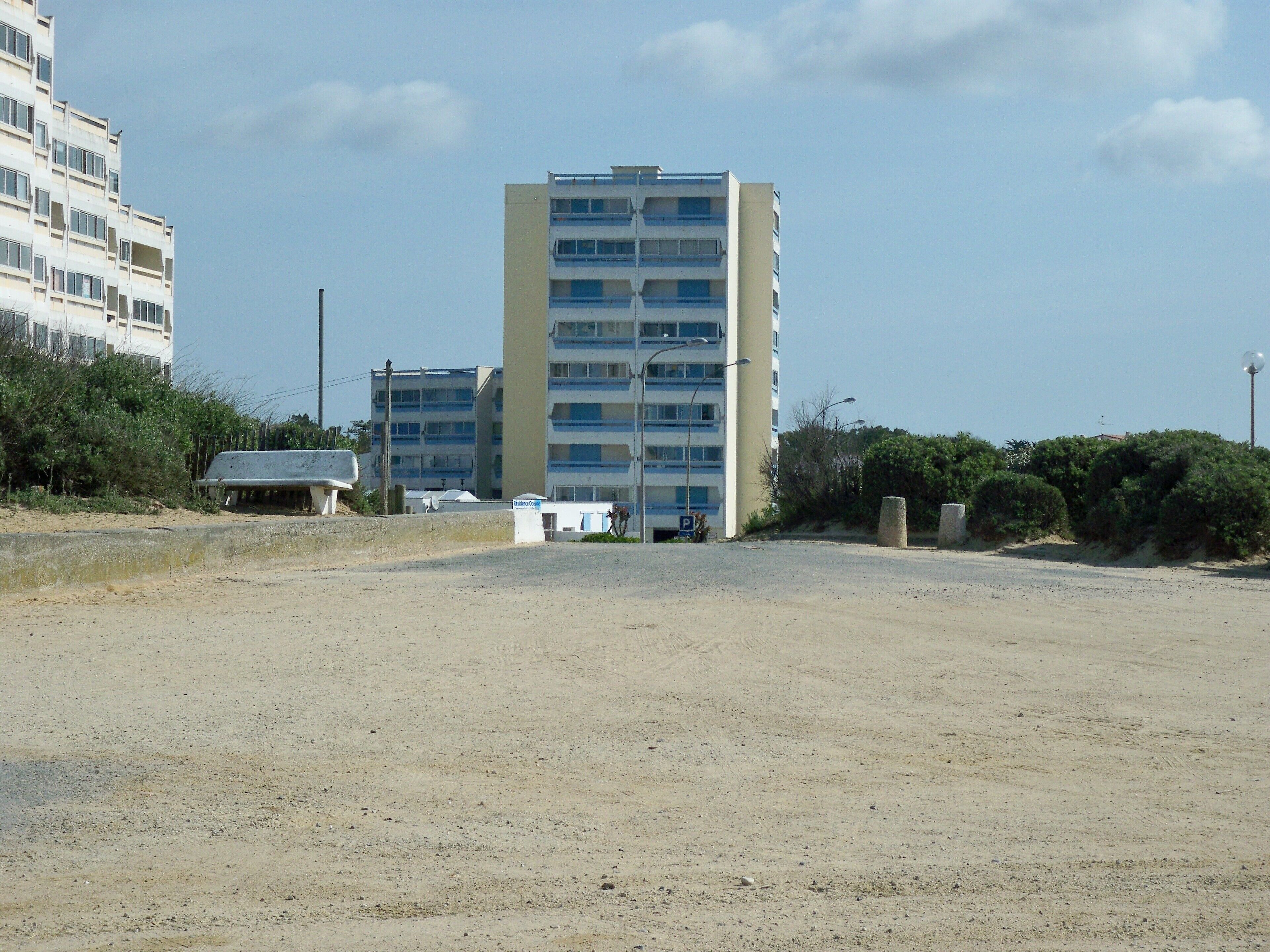 Ein mehrstöckiges Gebäude mit flacher Fassade, einem Parkplatz davor und einem wolkenlosen Himmel.