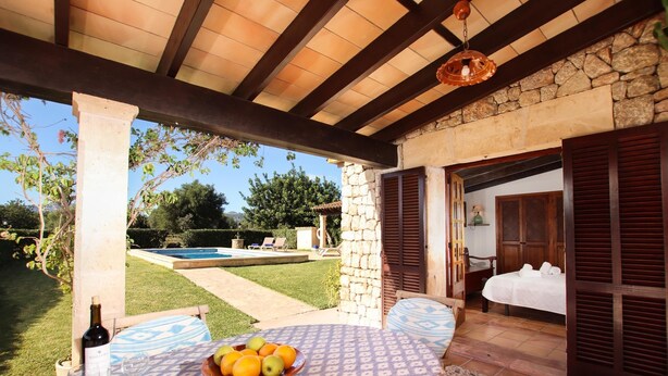 A covered outdoor seating area with a table set for two, a bottle of wine, and a bowl of fruit. - Finca with pool in calm area (Pollenca)