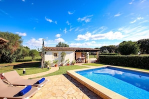 Uma piscina com espreguiçadeiras, uma casa pequena e um jardim.