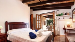 A neatly made bed with a white and blue blanket, a wooden nightstand with a lamp, and a wooden headboard. - Finca with pool in calm area (Pollenca)