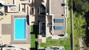 An aerial view of a residential property with a swimming pool, a patio area, and a covered outdoor seating space.