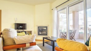 A modern living room with a sofa, a television, a fireplace, and a balcony with outdoor furniture.