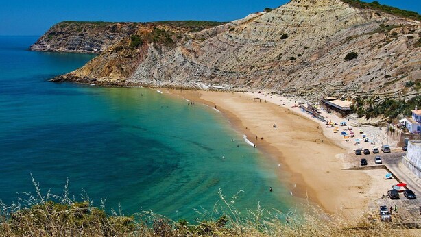 A coastal beach with clear turquoise waters, a sandy shore, and a rocky cliff.