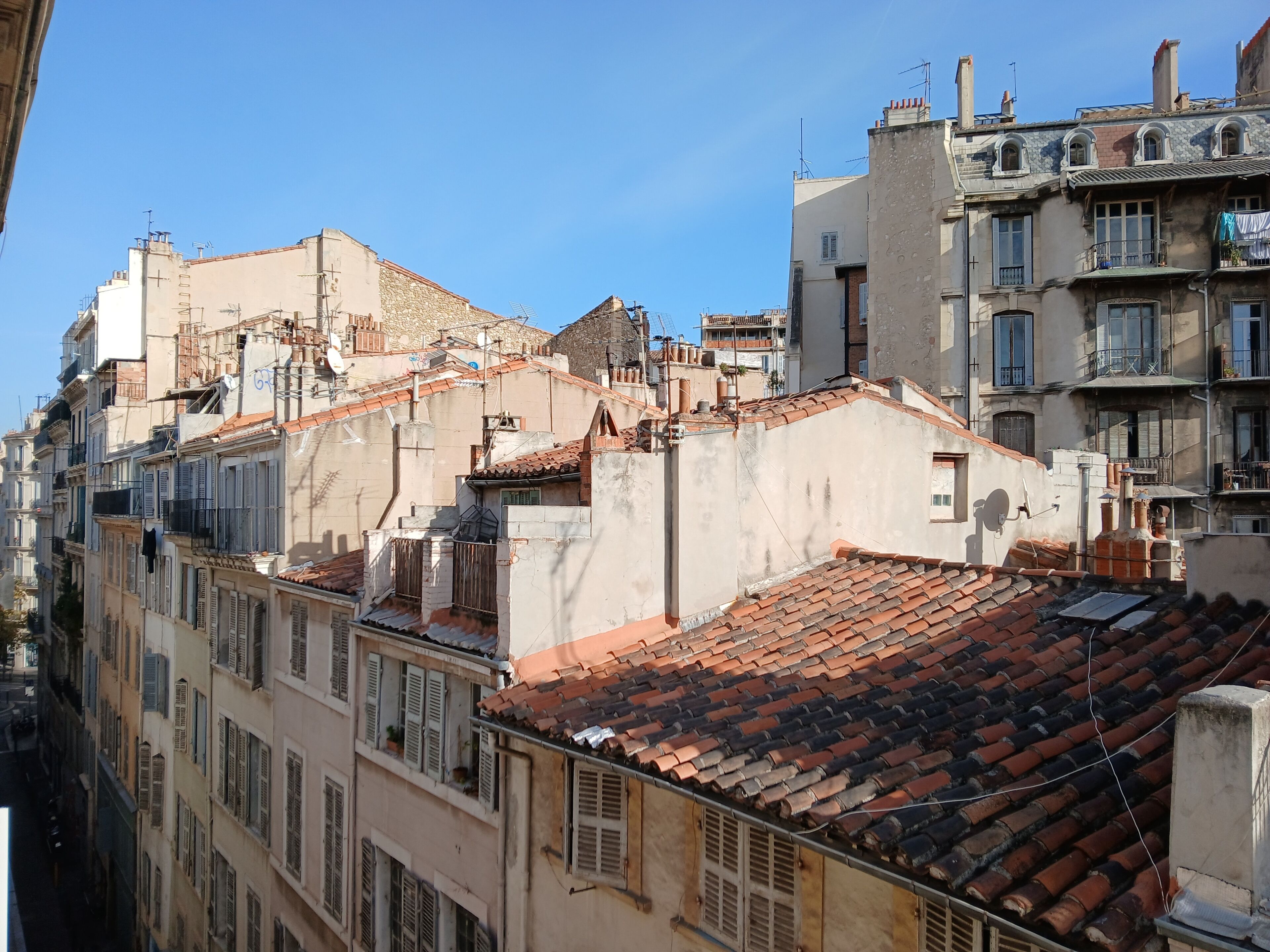 A row of multi-story buildings with red-tiled roofs, balconies, and various architectural styles.