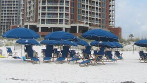 Un hotel de gran altura con múltiples balcones y una zona de playa con sombrillas y sillas de descanso.