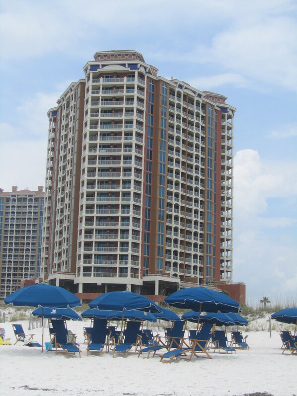 A high-rise hotel with multiple balconies and a beach area with sun umbrellas and lounge chairs.