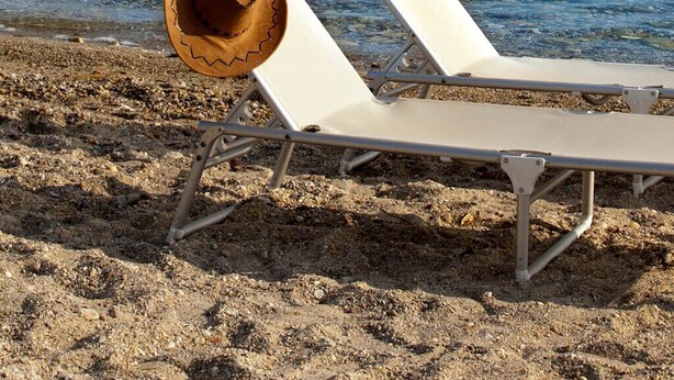 Una playa con una silla de playa blanca y un sombrero vaquero sobre la arena.