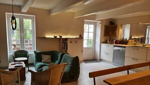 A cozy living room with a green sofa, wicker chairs, a wooden table, and a kitchen area with white cabinets and a dishwasher. - Large capacity houses in the village (Les Portes-En-Ré)