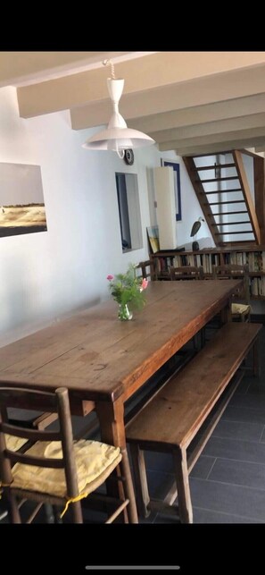 Een eetgedeelte met een houten tafel en banken, een hanglamp en een boekenkast met boeken.