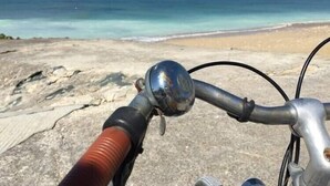 A bicycle with a metal handlebar and a red grip, positioned on a rocky beach with the ocean in the background. - Large capacity houses in the village (Les Portes-En-Ré)