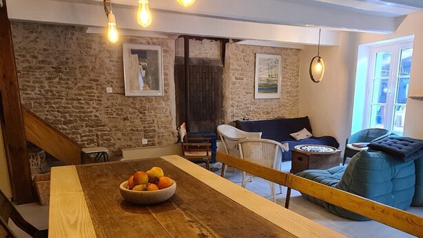 A rustic interior with a wooden dining table, a bowl of fruit, a blue sofa, and stone walls. - Large capacity houses in the village (Les Portes-En-Ré)