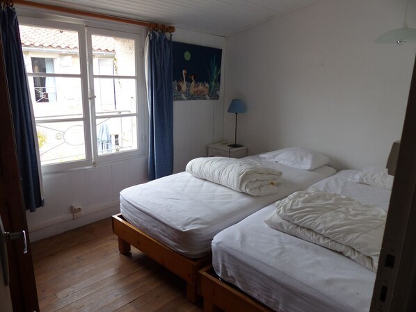 A bedroom with two beds, a window with curtains, a nightstand with a lamp, and a wall painting.