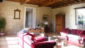 Un salón rústico con paredes de piedra, vigas de madera, un sofá rojo, una mesa de centro de vidrio y una ventana con vistas.
