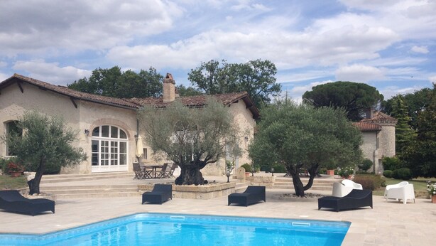 Una piscina con sillones de descanso y un edificio de piedra con techo de tejas.