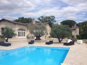 Une piscine avec des chaises longues et un bâtiment en pierre doté d’un toit en tuiles.
