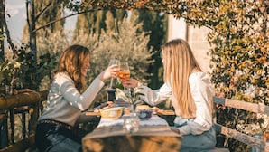 Two people toasting at a wooden table with a rustic setting, surrounded by greenery. - Asolo center, Free parking  (Asolo)