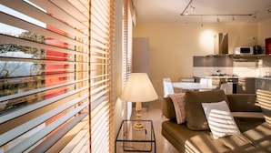 A modern living room with a sofa, a table with a lamp, and a view through large windows with blinds. - Asolo center, Free parking  (Asolo)