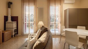 A living room with a sofa, a dining table with chairs, a lamp, a radiator, and a window with blinds. - Asolo center, Free parking  (Asolo)