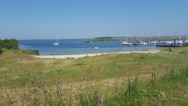 Un port de plaisance avec des bateaux amarrés, une plage de sable et des espaces couverts d’herbe.