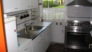 Une cuisine de taille réduite, avec des meubles blancs, un évier en acier inoxydable et une cuisinière à gaz.