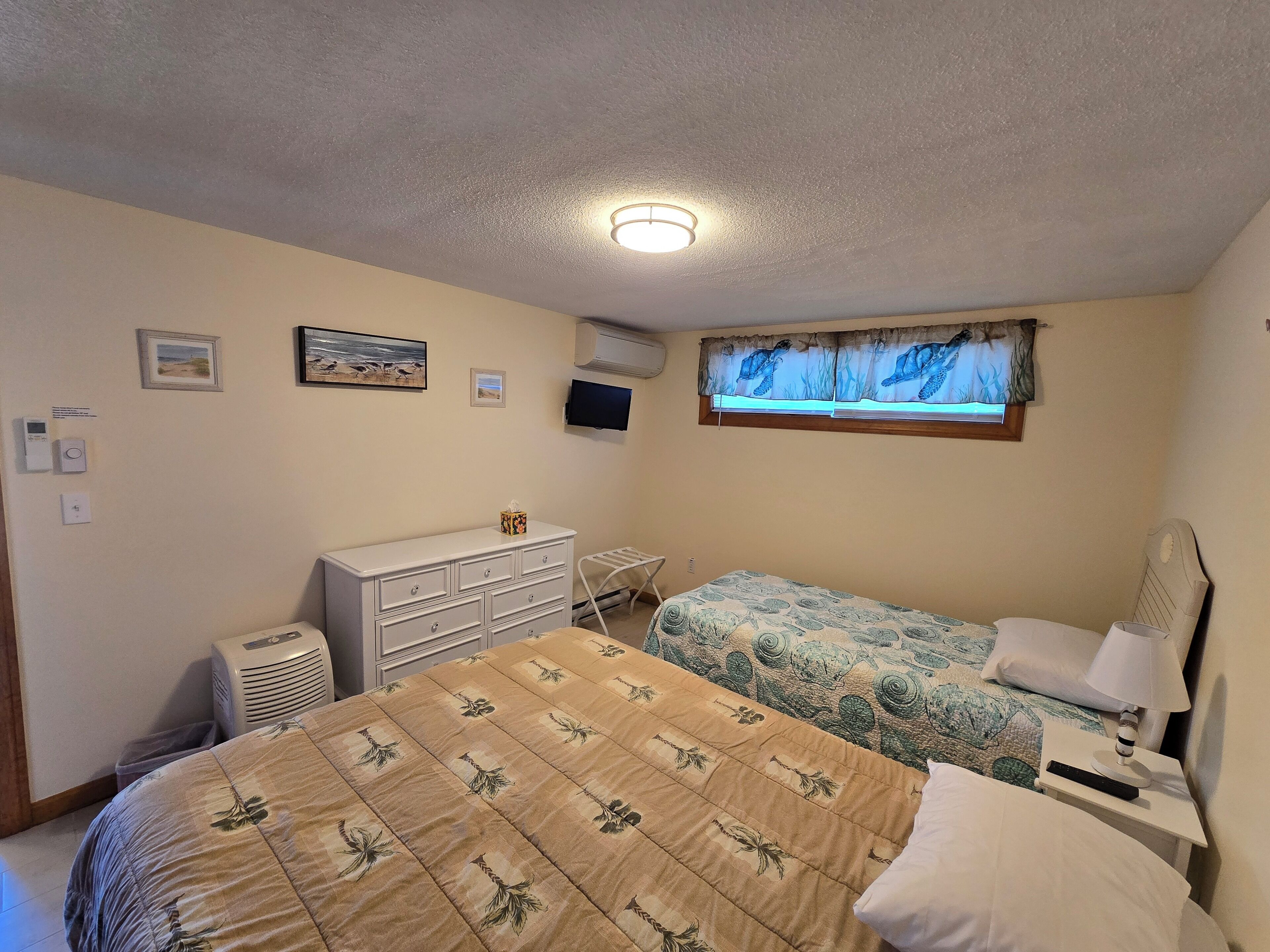 A bedroom with a bed, a dresser, a TV, and a window with curtains.