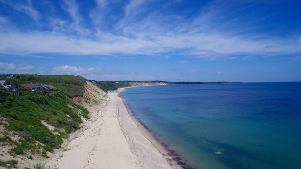 Uma estrada costeira que leva a uma praia, com casas numa encosta.