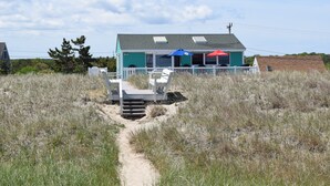 Uma casa de praia com varanda, um pequeno deck e um caminho que leva à entrada.