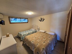 Une chambre avec deux lits, un bureau, une fenêtre avec des rideaux, un luminaire au plafond et un élément de décoration murale.