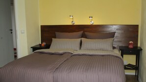 A neatly made bed with a brown comforter and pillows, two bedside lamps, and a small nightstand with a book and a red object.