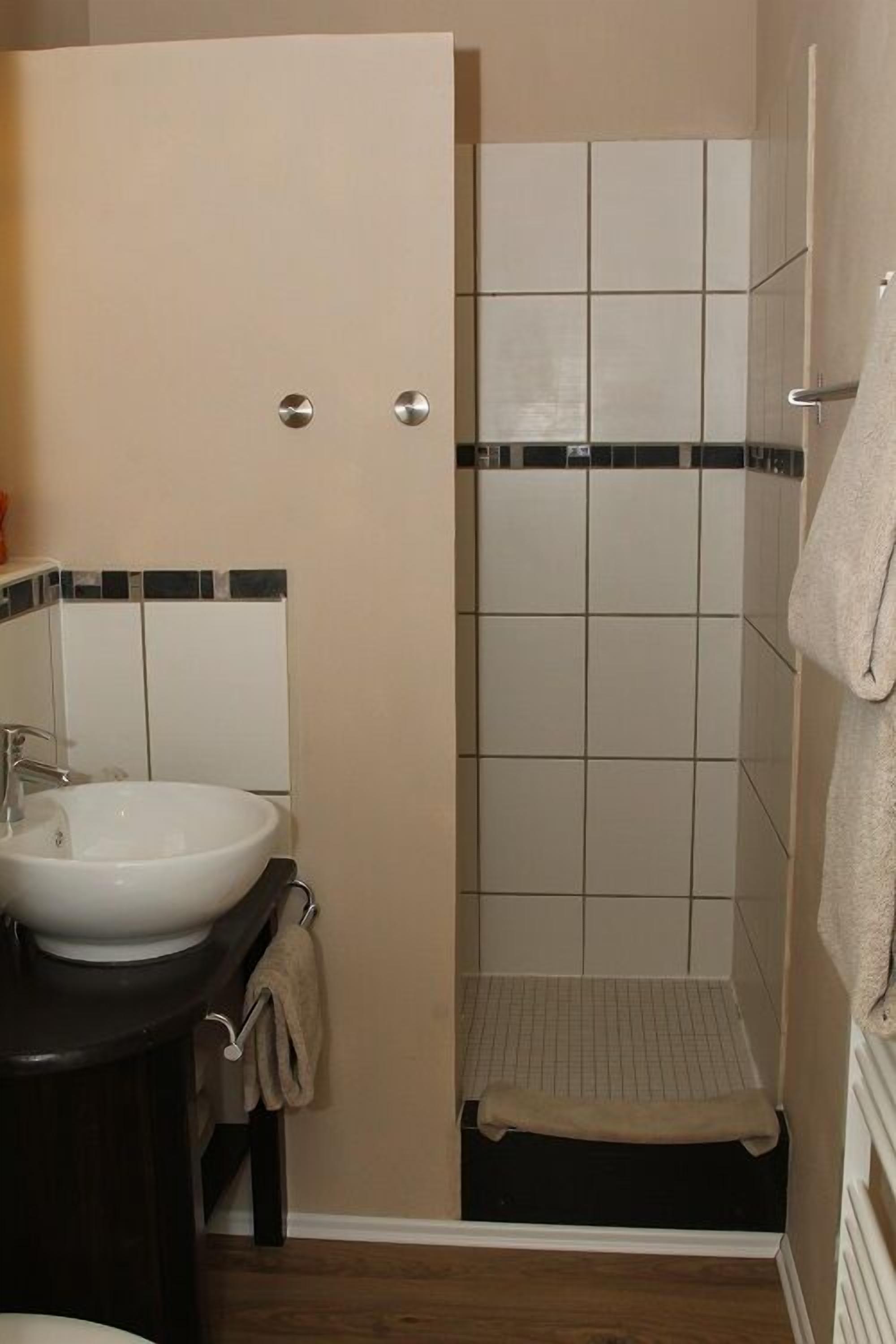 A bathroom with a white sink, a mirror, and a shower area with tiled walls and floor.
