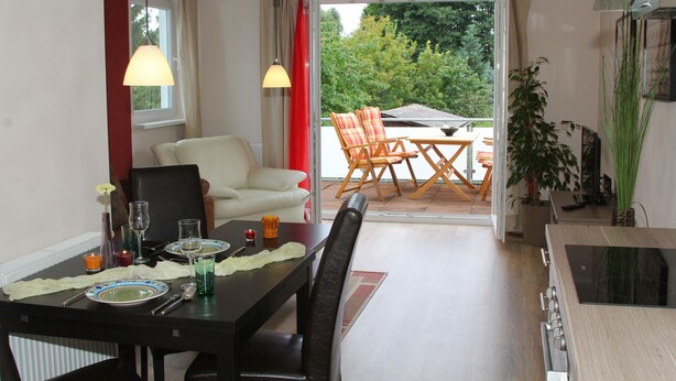 A dining area with a table set for two, a sofa, and a view of the outdoors.