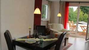A dining area with a table set for four, chairs, a window with curtains, and a view of greenery outside.