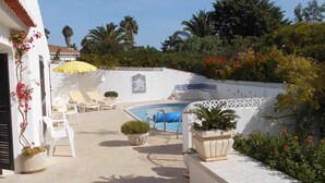 Zona de piscina amb gandules, un parasol groc i plantes decoratives.