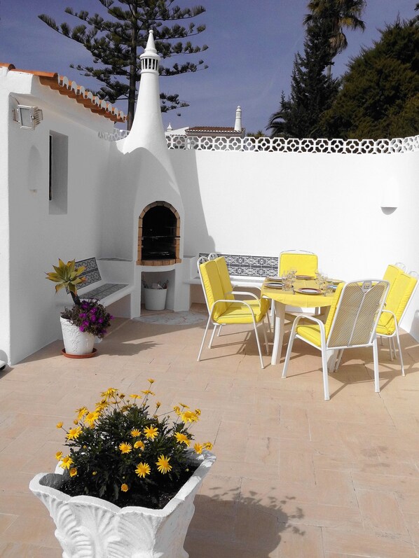 An outdoor patio with a white wall, a small archway, a table with yellow chairs, and a potted plant with yellow flowers. - Villa 185m², 3000m² garden, private pool, 5 min. to beach, WLAN, domestic help (Carvoeiro)