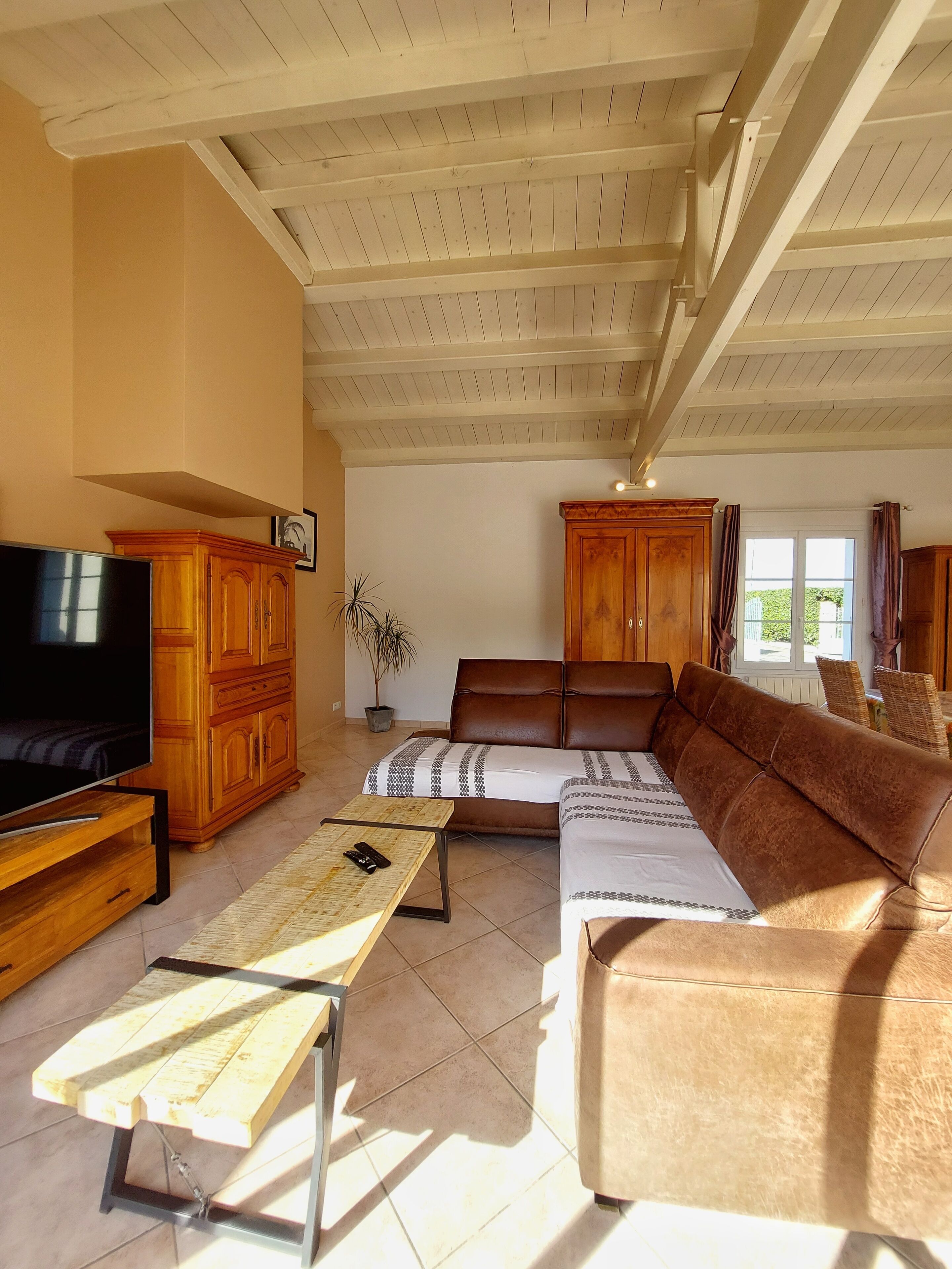 Ein Wohnzimmer mit Fernseher, Holzschränken, einer Couch und einem Essbereich mit Tisch und Stühlen.