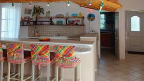 A kitchen with a high ceiling, a thatched roof, and a bar area with colorful chairs.