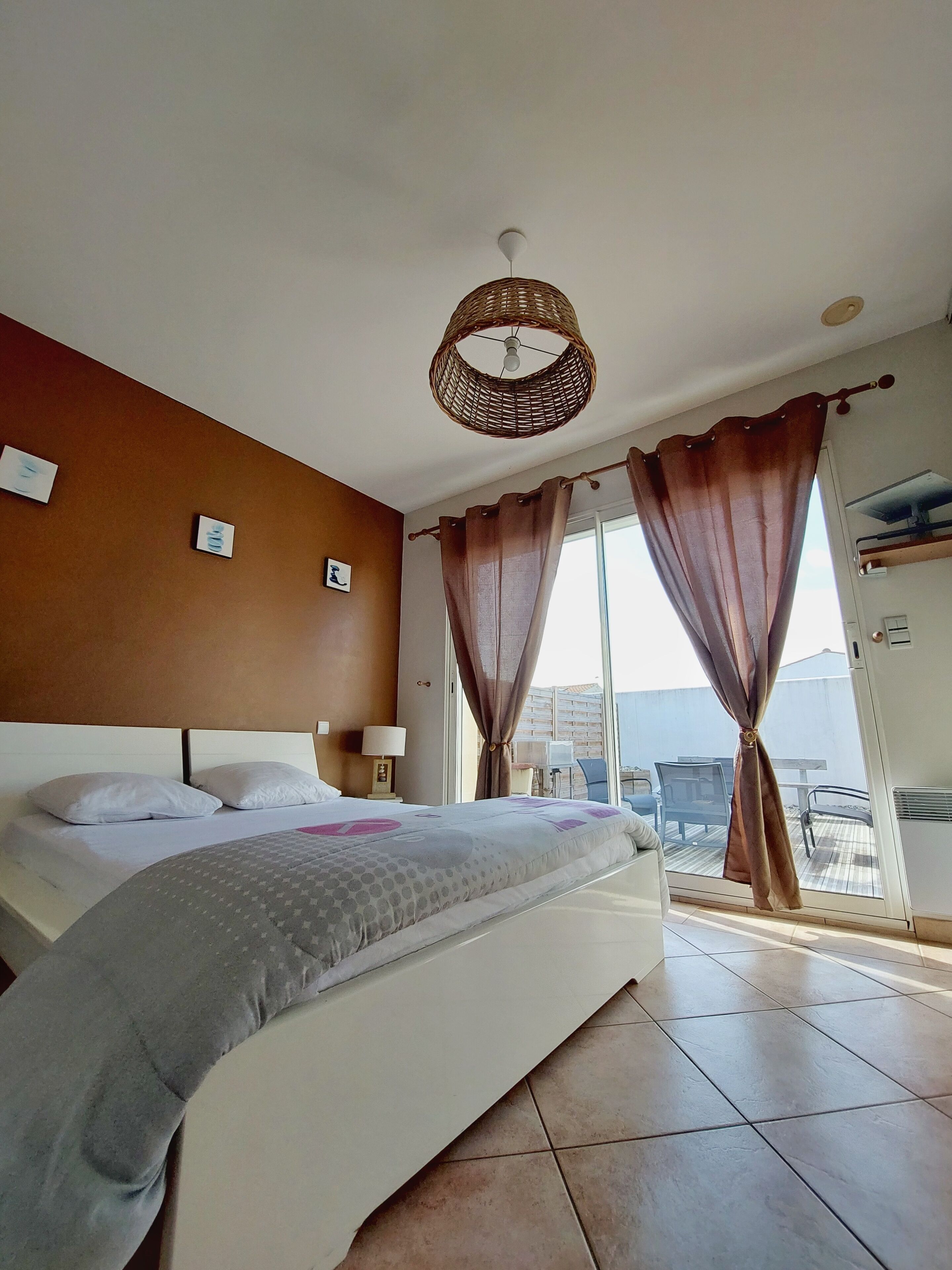 Habitación de hotel con una cama grande, una lámpara de techo de mimbre y un balcón con vistas.