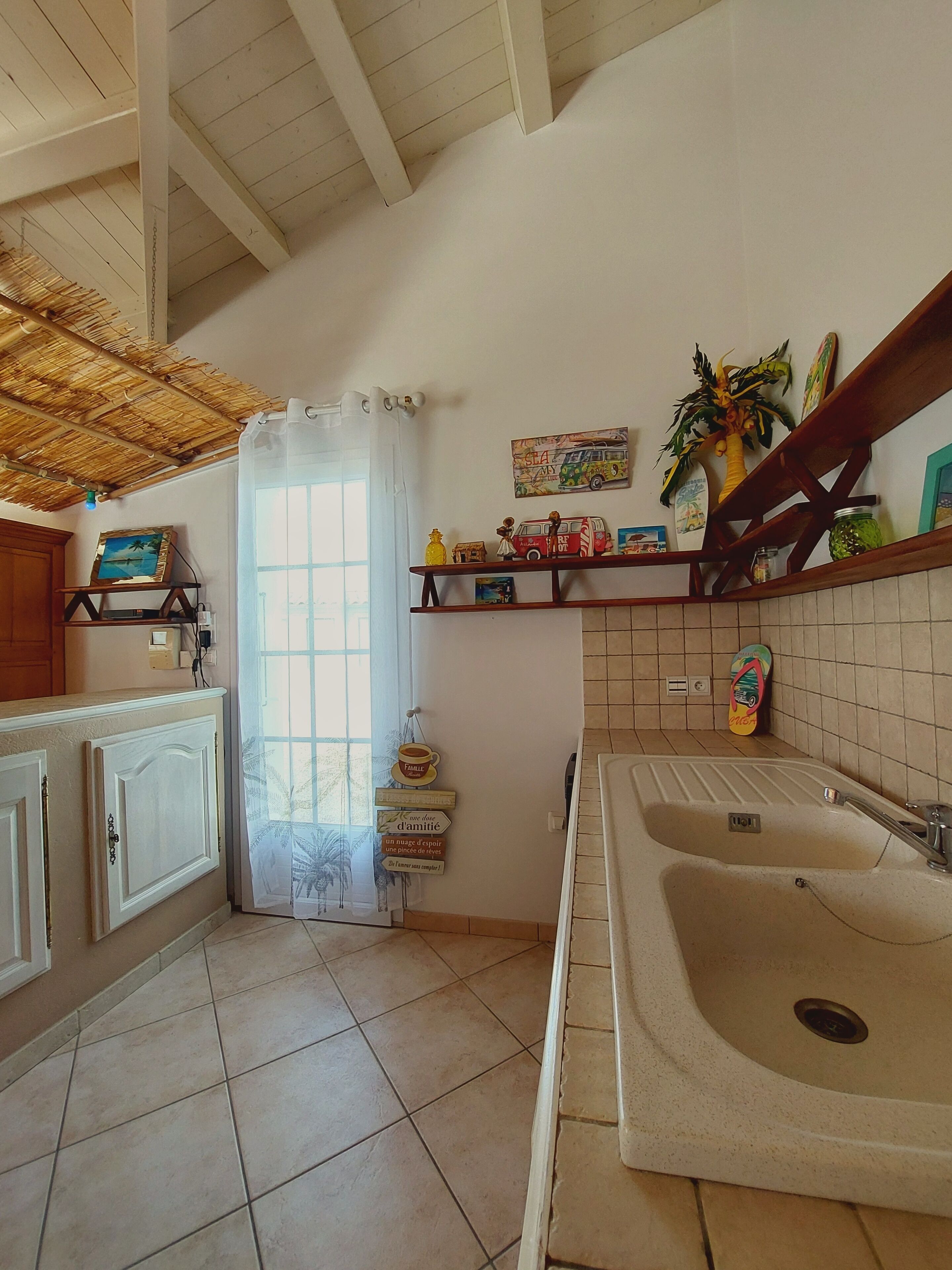 Una cocina con un lavamanos grande, armarios de madera, piso de baldosas y techo de paja.