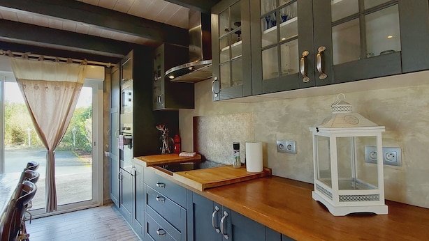 A modern kitchen with dark cabinets, a wooden countertop, and a view to the outside.