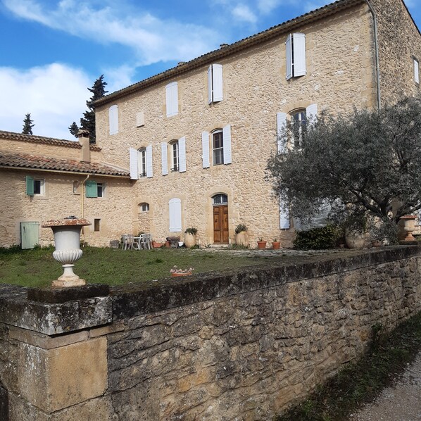 A stone building with multiple windows and a door, surrounded by a stone wall and greenery.