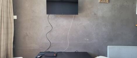 Habitació amb televisió penjada, un moble negre per a entreteniment amb un calaix, un otomà blanc i una obra d'art penjada a la paret.