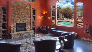 A spacious living room with a stone fireplace, comfortable seating, and a view of a hot tub and garden. - Gated La Paloma Home, Private Lot with City & Mountain views (Tucson)