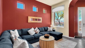 A modern living room with a dark blue sectional sofa, a round wooden coffee table, and a red accent wall. - Gated La Paloma Home, Private Lot with City & Mountain views (Tucson)