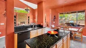 A modern kitchen with granite countertops, a central island, and a dining area with a large window overlooking a patio. - Gated La Paloma Home, Private Lot with City & Mountain views (Tucson)